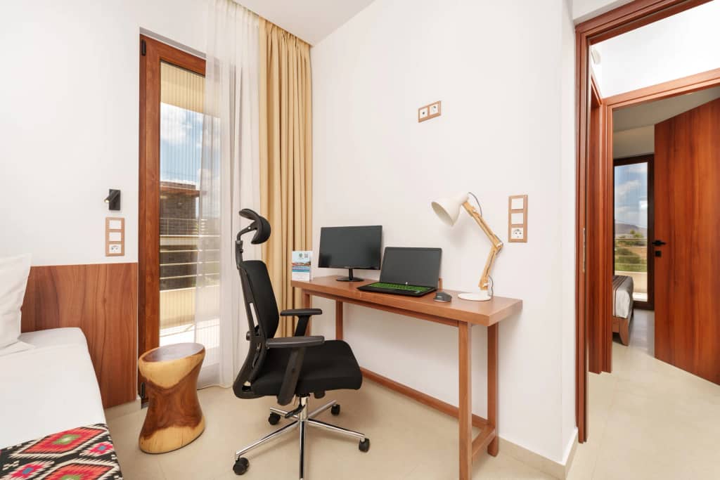 In-suite workstation with monitor, desk lamp and ergonomic office chair at Volta Suites and Villas