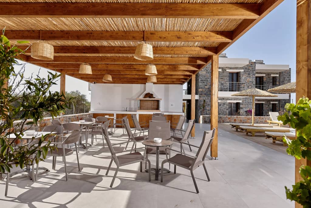 Shaded communal terrace with wicker pendant lights, cafe tables and stone-built suites of Volta Stay behind