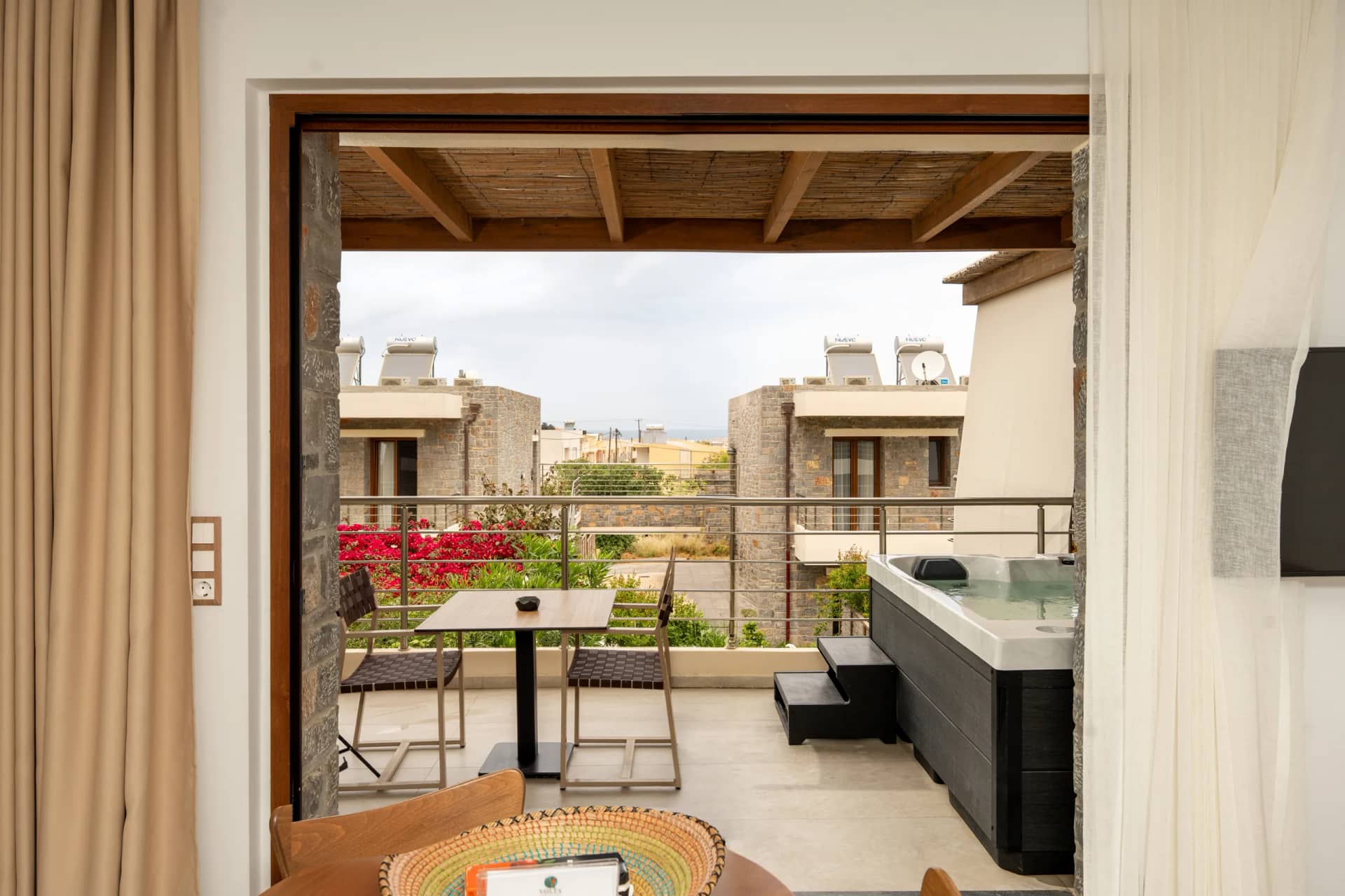 Suite interior opening to a balcony with hot tub, cafe table and views of stone villas and greenery